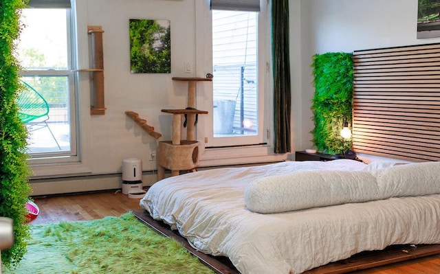 bedroom with multiple windows, a baseboard radiator, and wood finished floors