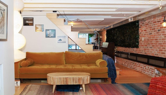 living room with brick wall, stairway, and wood finished floors