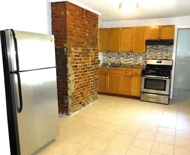 kitchen with under cabinet range hood, a sink, appliances with stainless steel finishes, backsplash, and brown cabinets