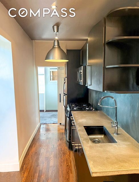 kitchen with appliances with stainless steel finishes, a sink, light countertops, wood finished floors, and baseboards