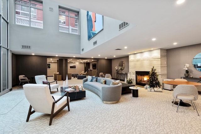 living area featuring a large fireplace, a high ceiling, visible vents, and carpet flooring