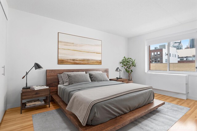 bedroom with light wood-style flooring, a view of city, and baseboards