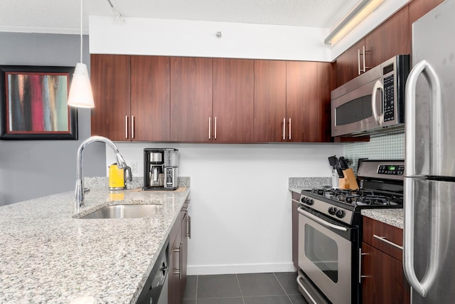 kitchen featuring light stone counters, stainless steel appliances, dark tile patterned flooring, a sink, and baseboards