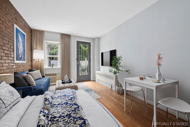 living room featuring radiator, brick wall, baseboards, a wall mounted air conditioner, and wood finished floors