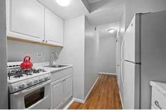 kitchen featuring white appliances, white cabinets, wood finished floors, and a sink