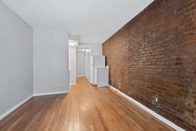 unfurnished room featuring baseboards, wood-type flooring, and brick wall