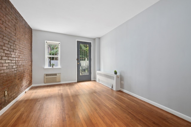 empty room featuring baseboards, wood-type flooring, radiator, and a wall unit AC