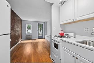 kitchen with brick wall, light countertops, wood finished floors, white cabinets, and white appliances