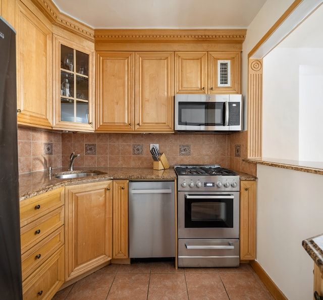 kitchen featuring light stone counters, appliances with stainless steel finishes, a sink, backsplash, and light tile patterned flooring