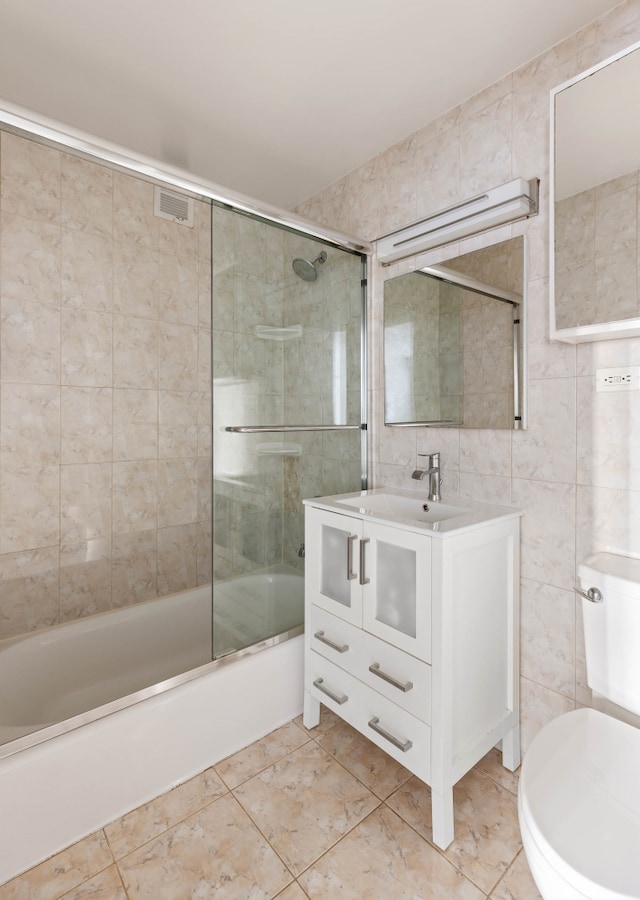 bathroom featuring visible vents, tile walls, toilet, and bath / shower combo with glass door