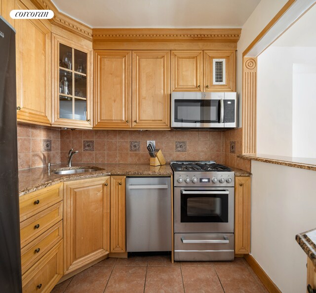 kitchen featuring light tile patterned flooring, stainless steel appliances, a sink, decorative backsplash, and light stone countertops