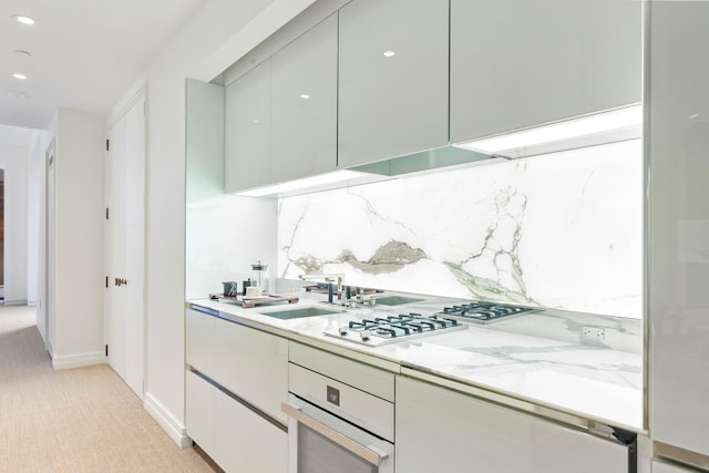 kitchen featuring gas cooktop, white oven, modern cabinets, light colored carpet, and backsplash