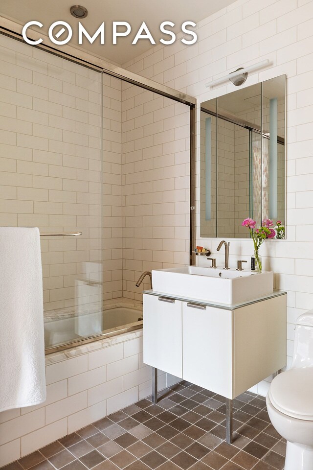 full bath featuring tile walls, tiled shower / bath, toilet, vanity, and tile patterned floors