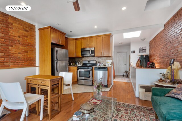 kitchen with a skylight, stainless steel appliances, visible vents, light wood-style flooring, and brick wall