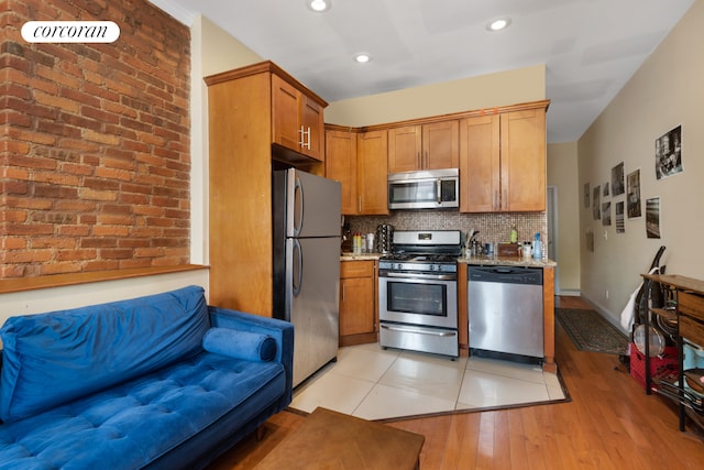 kitchen featuring light wood-style flooring, light stone countertops, appliances with stainless steel finishes, backsplash, and brown cabinets