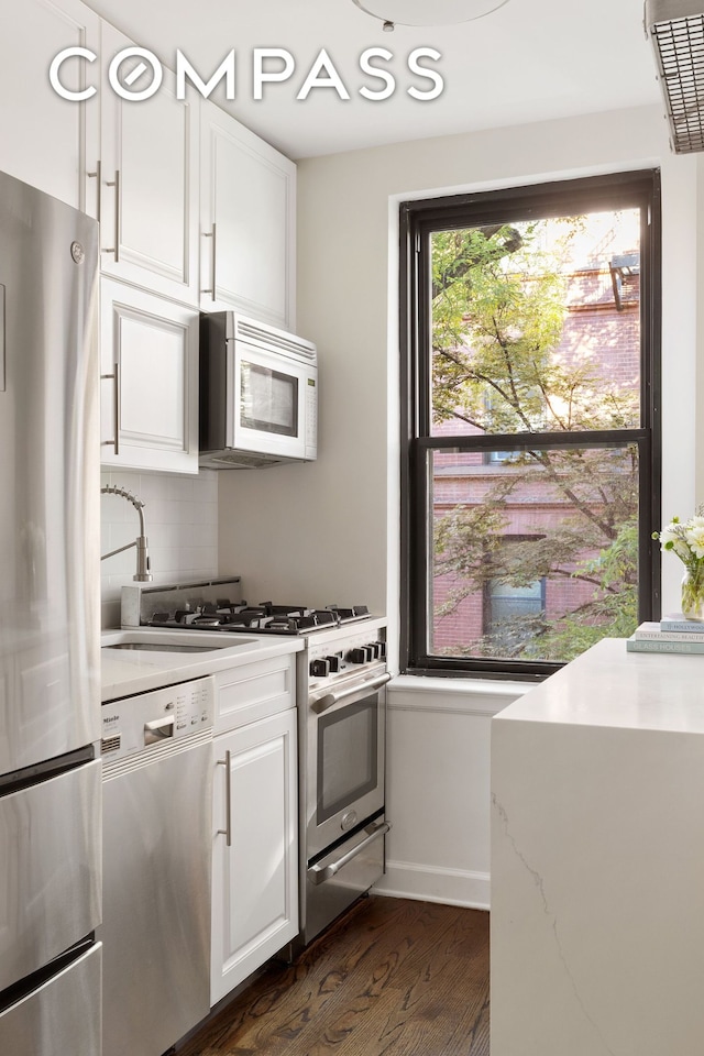 kitchen with baseboards, dark wood finished floors, white cabinets, appliances with stainless steel finishes, and tasteful backsplash