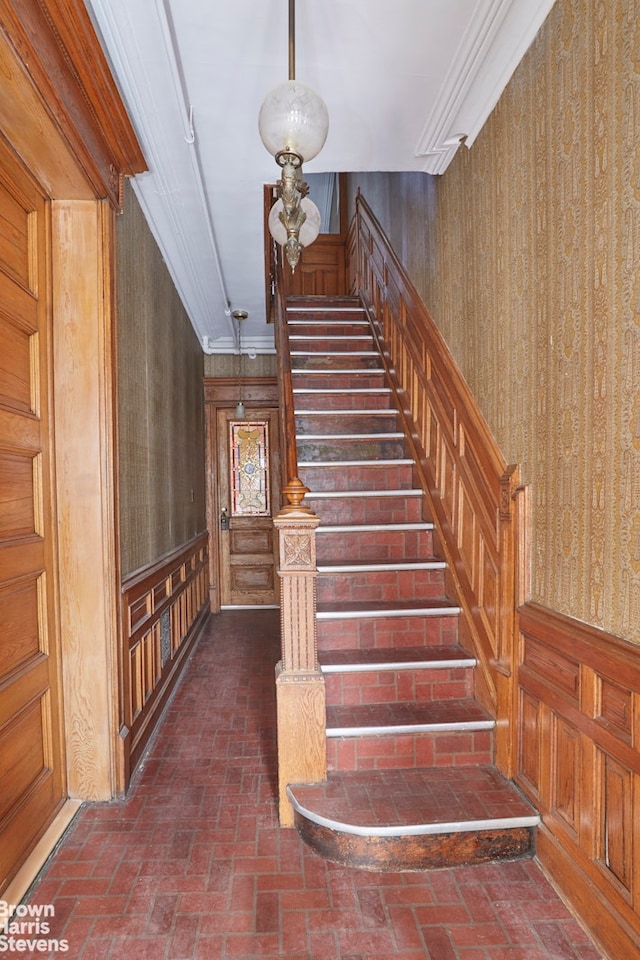 stairway featuring wooden walls, brick floor, and crown molding