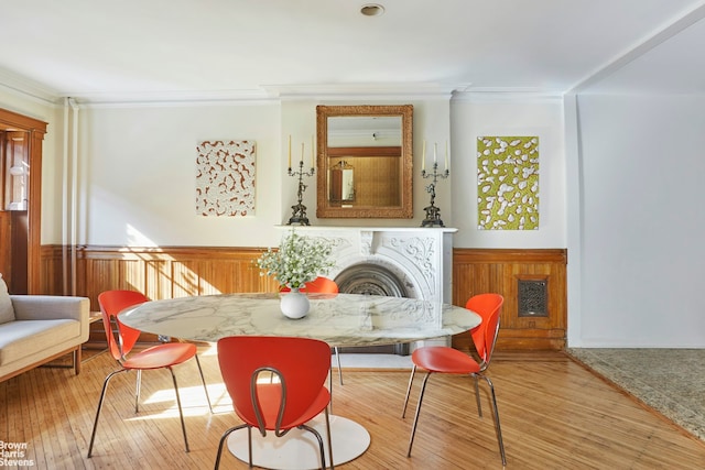 dining room featuring ornamental molding, a wainscoted wall, a tiled fireplace, and hardwood / wood-style flooring