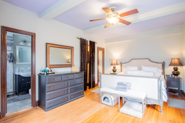 bedroom with beam ceiling, connected bathroom, light wood finished floors, ceiling fan, and a wood stove