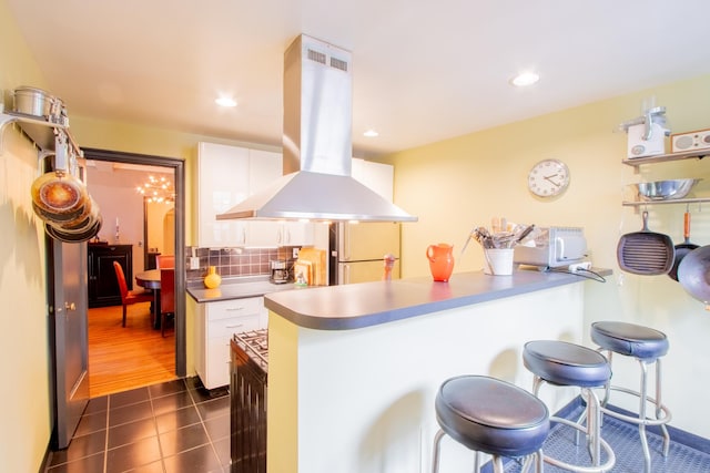 kitchen with a kitchen bar, decorative backsplash, island exhaust hood, freestanding refrigerator, and white cabinets