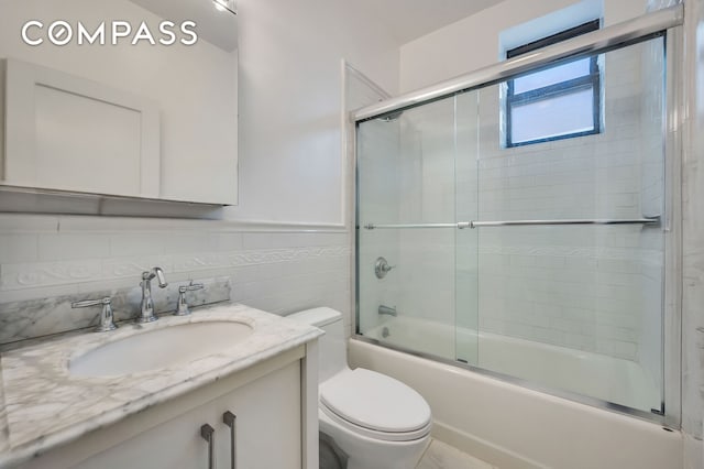 full bathroom featuring toilet, tile walls, wainscoting, enclosed tub / shower combo, and vanity