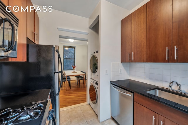 kitchen with stacked washer and dryer, a sink, black microwave, light tile patterned floors, and dishwasher