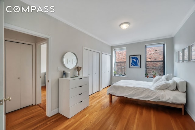 bedroom with two closets, baseboards, light wood finished floors, and ornamental molding