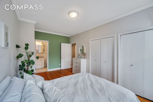 bedroom featuring wood finished floors, baseboards, ornamental molding, multiple closets, and ensuite bathroom