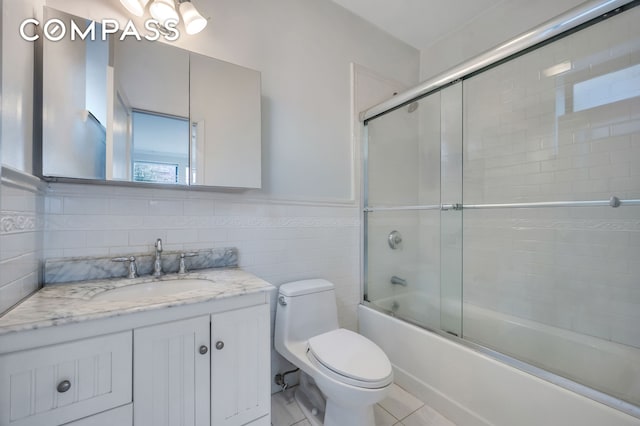 full bathroom with toilet, vanity, wainscoting, shower / bath combination with glass door, and tile walls