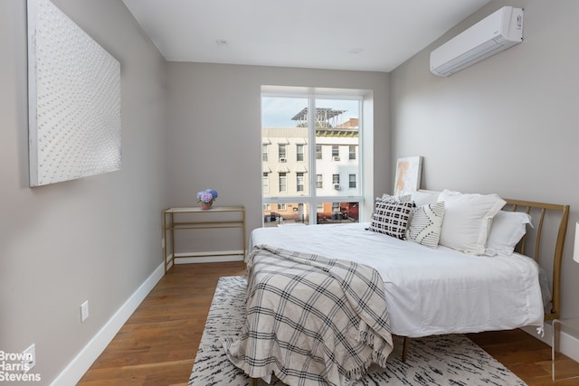 bedroom with a wall mounted air conditioner, baseboards, and wood finished floors