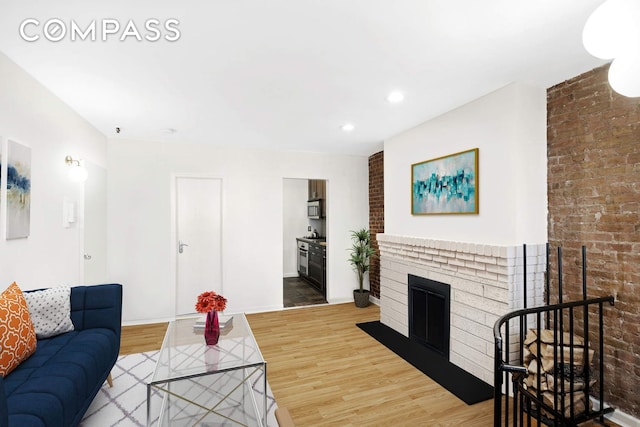 living room featuring a brick fireplace, brick wall, baseboards, and wood finished floors