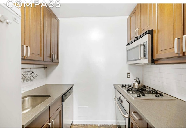 kitchen featuring baseboards, brown cabinetry, appliances with stainless steel finishes, a sink, and backsplash