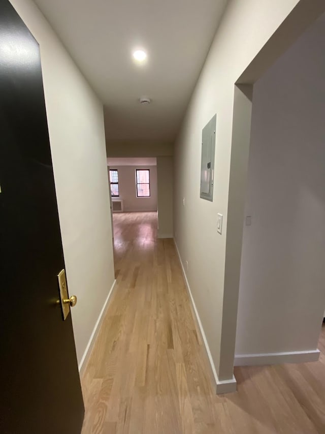 corridor featuring light wood-type flooring, electric panel, and baseboards