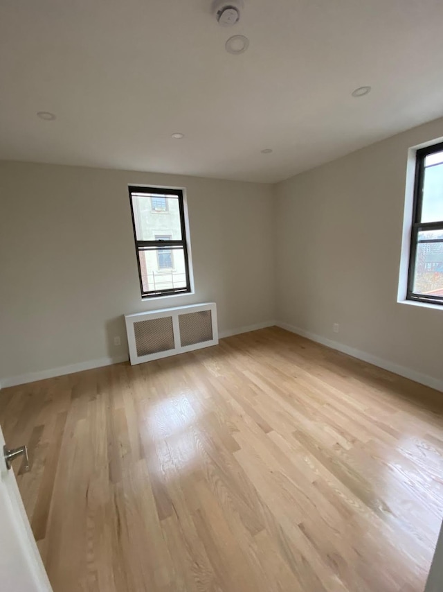 empty room featuring radiator, light wood-style flooring, and baseboards