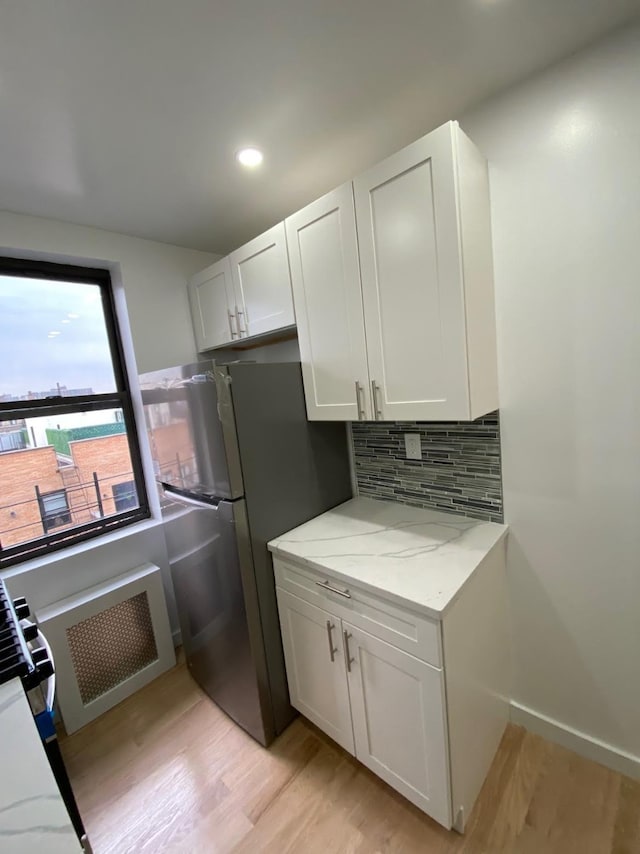 kitchen featuring tasteful backsplash, freestanding refrigerator, white cabinetry, and light stone countertops