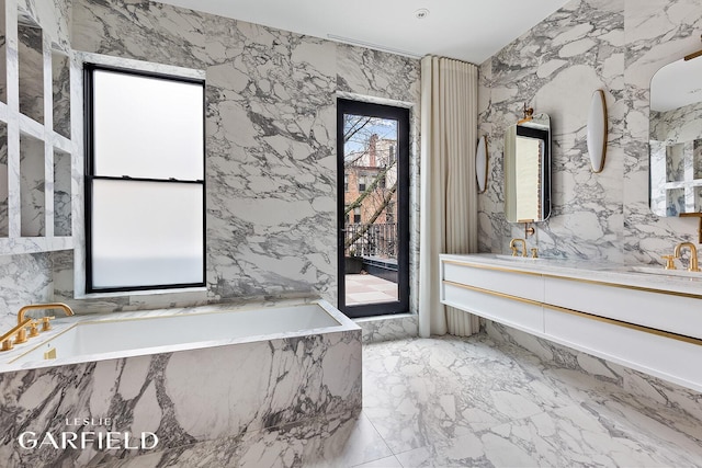 bathroom featuring marble finish floor, double vanity, stone wall, a sink, and a bath