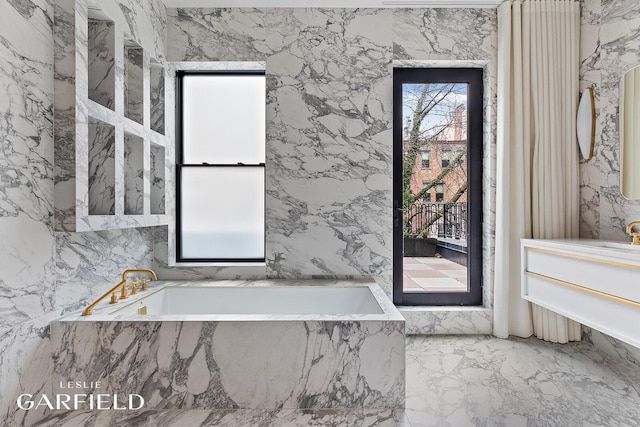 full bathroom featuring stone wall, marble finish floor, vanity, and a bath