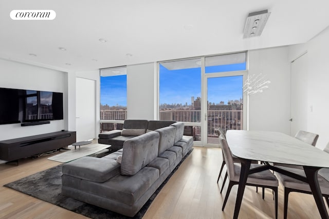 living area with a view of city, a wall of windows, light wood-style flooring, and visible vents