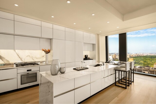 53 W 53rd St Unit 49A, New York City, NY 10019 - kitchen featuring stainless steel gas stovetop, white cabinets, light wood-style flooring, oven, and modern cabinets