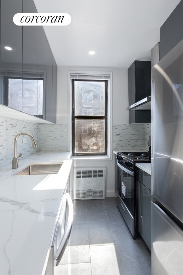 kitchen featuring modern cabinets, freestanding refrigerator, light stone countertops, a sink, and gas stove