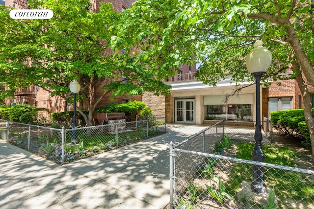 view of property hidden behind natural elements featuring a balcony, stone siding, a fenced front yard, and brick siding