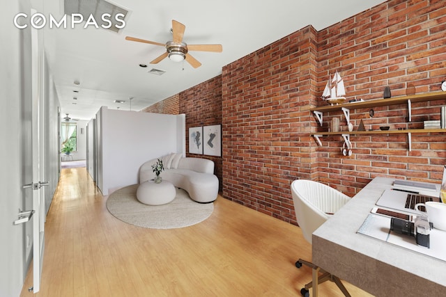 office space featuring a ceiling fan, visible vents, brick wall, and wood finished floors