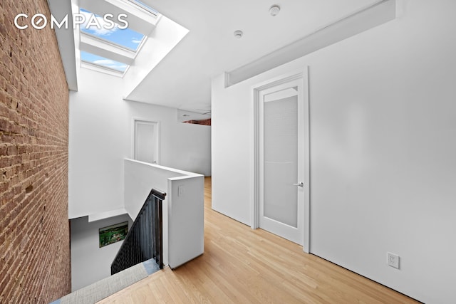 unfurnished office featuring brick wall, a skylight, and light wood-style floors