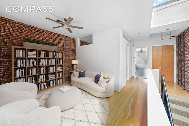 living area featuring a ceiling fan, brick wall, and wood finished floors