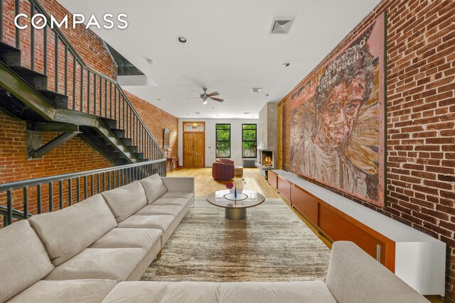 living area with visible vents, a fireplace, brick wall, and wood finished floors