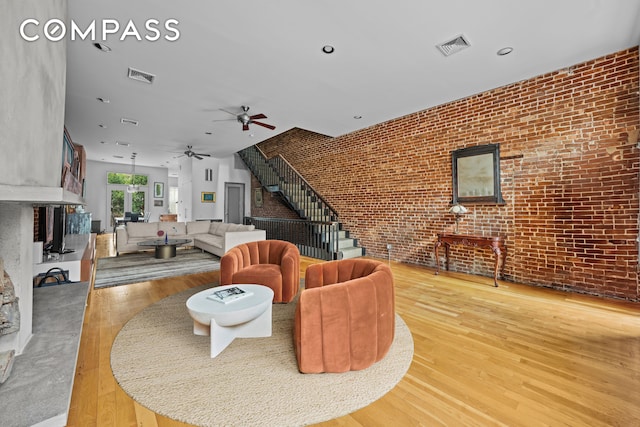 living room with visible vents, brick wall, a fireplace, and wood finished floors