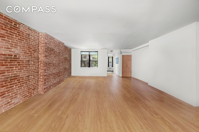 unfurnished living room with brick wall and wood finished floors