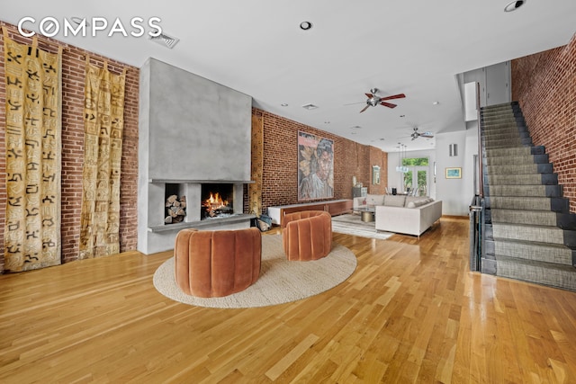 living room featuring light wood finished floors, visible vents, brick wall, stairway, and a warm lit fireplace