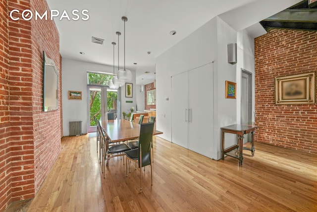 dining area with brick wall, radiator heating unit, visible vents, and light wood-style floors