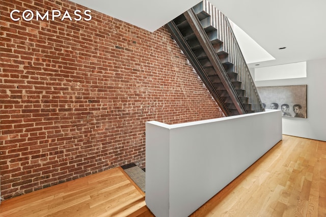 corridor featuring brick wall, stairway, and wood finished floors